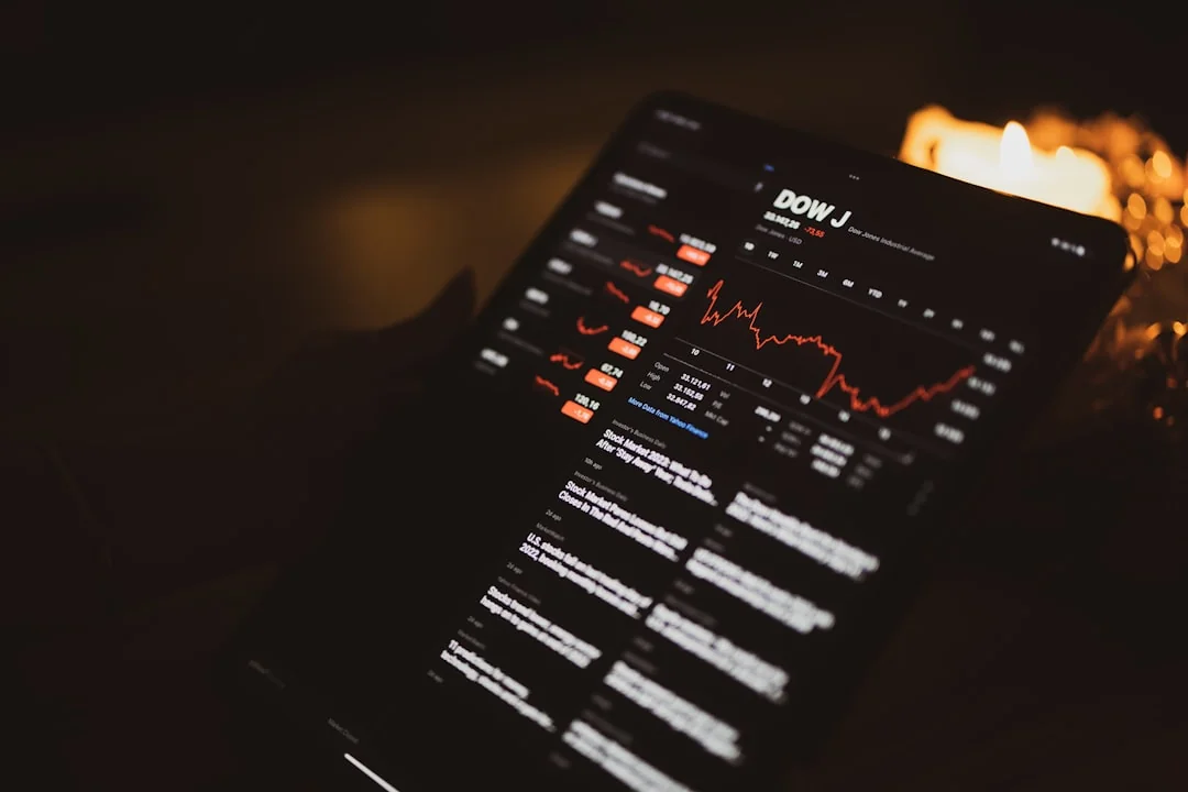 Two businessmen analyze stock market data using a smartphone and laptop in a modern office setting.